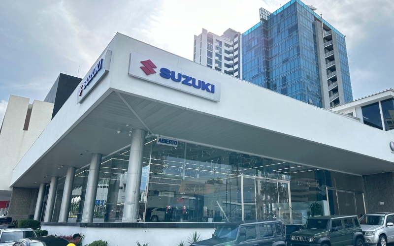Edificio moderno con el logo de Suzuki en la entrada y varios vehículos de la marca expuestos en la parte delantera.